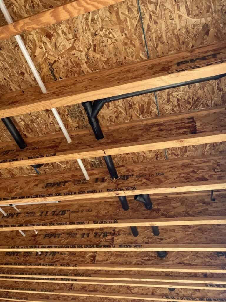 Black and white plumbing pipes installed in ceiling framing.